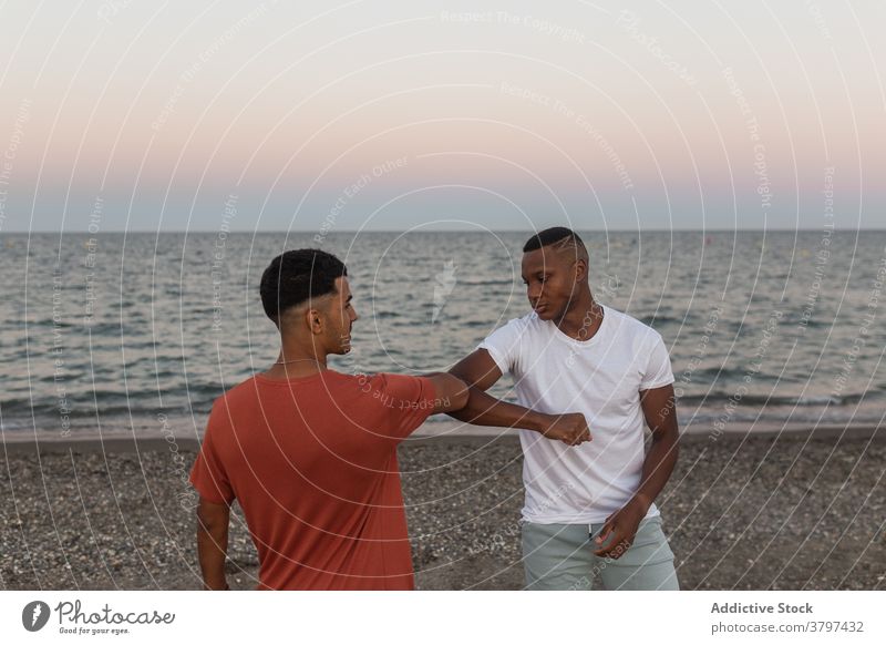 Stilvolle schwarze Freunde stoßen Ellenbogen auf Meer Ufer in Abend Ellbogen Gruß stylisch Haarschnitt Strand Himmel Sonnenuntergang Männer Afroamerikaner