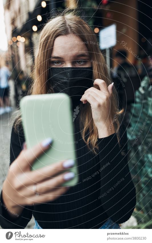 Junge Frau führt Videoanrufgespräche, während sie mit der Gesichtsmaske in der Innenstadt läuft, um eine Virusinfektion zu vermeiden Anruf Pflege Kaukasier