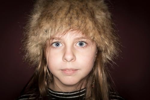 Studioporträt eines süßen Mädchens mit langen blonden Haaren, das einen Winterhut vor braunem Hintergrund trägt hübsches Mädchen Atelier-Portrait Hut Europäer