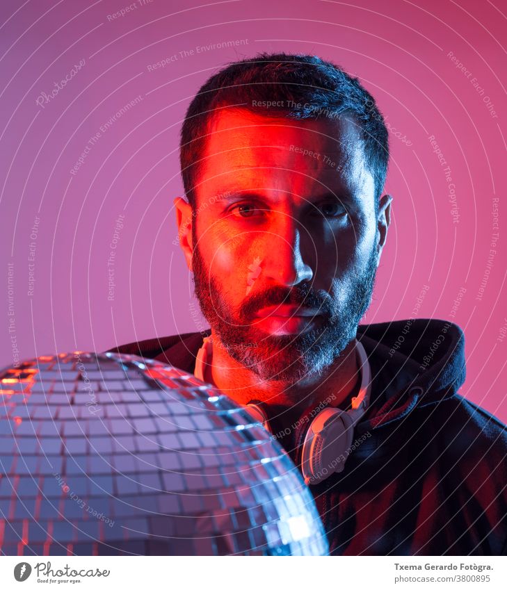 Buntes Studioporträt eines bärtigen DJs mit Kopfhörern vor rot-blauem Hintergrund. deejay Disco-Musik farbig Pop Klang Discokugel Spiegel clubbing farbenfroh