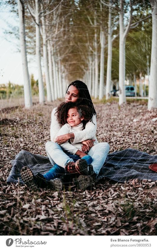hispanische Mutter und Afrokindermädchen im Freien, die sich in der Natur entspannen. Herbstsaison. Familienkonzept Tochter gemischte Rasse Afro-Look