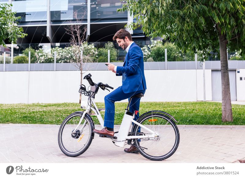 Stilvolle männliche Führungskraft plaudert auf Smartphone in der Nähe von Elektrofahrrad Exekutive Textnachrichten elektrisch Fahrrad stylisch Bekleidung