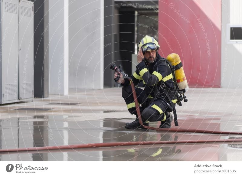 Feuerwehrmann in Uniform auf nassem Bürgersteig in der Nähe von Schlauch Schutzhelm Sicherheit Beruf beschaulich Reflexion & Spiegelung Straßenbelag Gerät