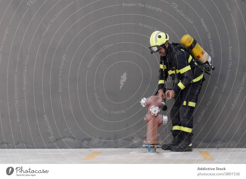 Feuerwehrmann in Uniform mit Ausrüstung in der Nähe von Feuer Hydrant Gerät Beruf Routine üben Feuerlöscher Wand Straßenbelag Beton Mann Arbeit Schutzhelm