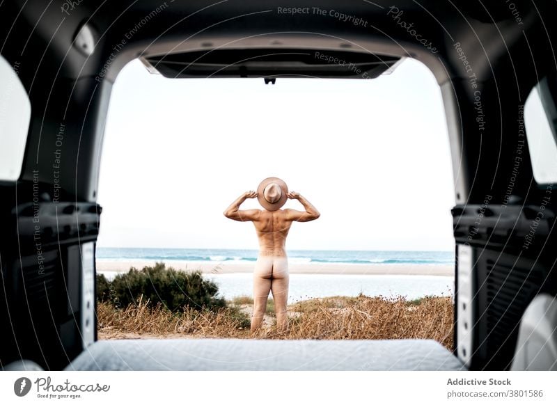 Anonymer nackter Mann mit ausgestreckten Armen in Aufregung am Meeresufer ausdehnen Freiheit Meeresküste Freude reisen aufgeregt Stiefel PKW Autoreise Hut