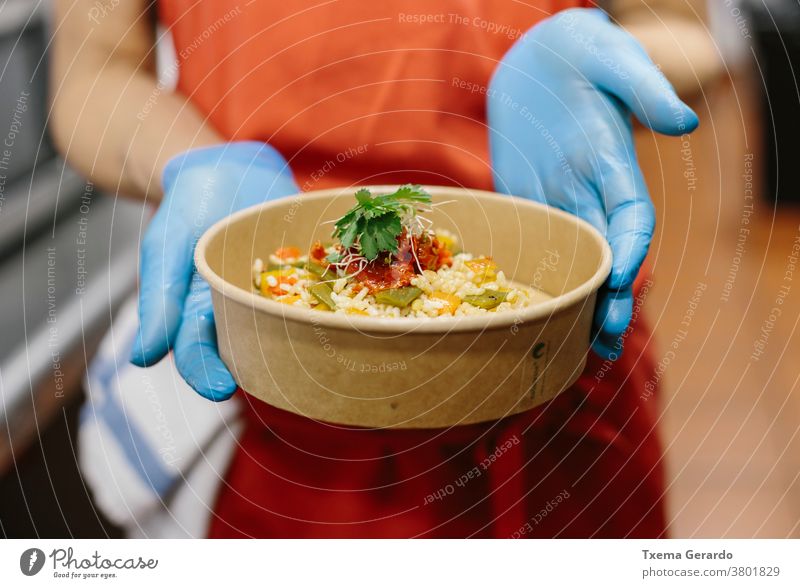 Eine Köchin präsentiert ihren Gourmet-Reissalat in einem kompostierbaren Take-away-Behälter Essen zum Mitnehmen Salatbeilage Koch Vegetarier Veganer Container