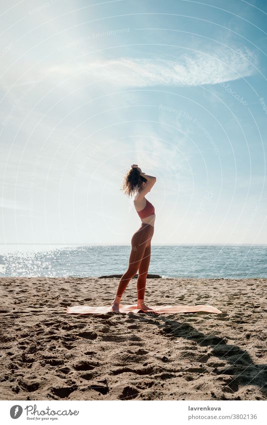 Junge erwachsene Frau, die vor ihrer Yogapraxis am Strand einen Pferdeschwanz macht, selektiver Fokus Himmel im Freien Übung jung Wohlgefühl Zen Energie passen