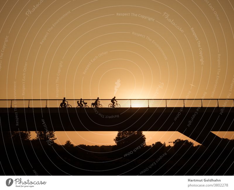 Silhouetten einer Gruppe Fahrradfahrer die kurz vor Sonnenuntergang über eine Brücke fahren. Ausflug bauwerk Fahrad fahren Fahrräder fahrzeug Familie freizeit