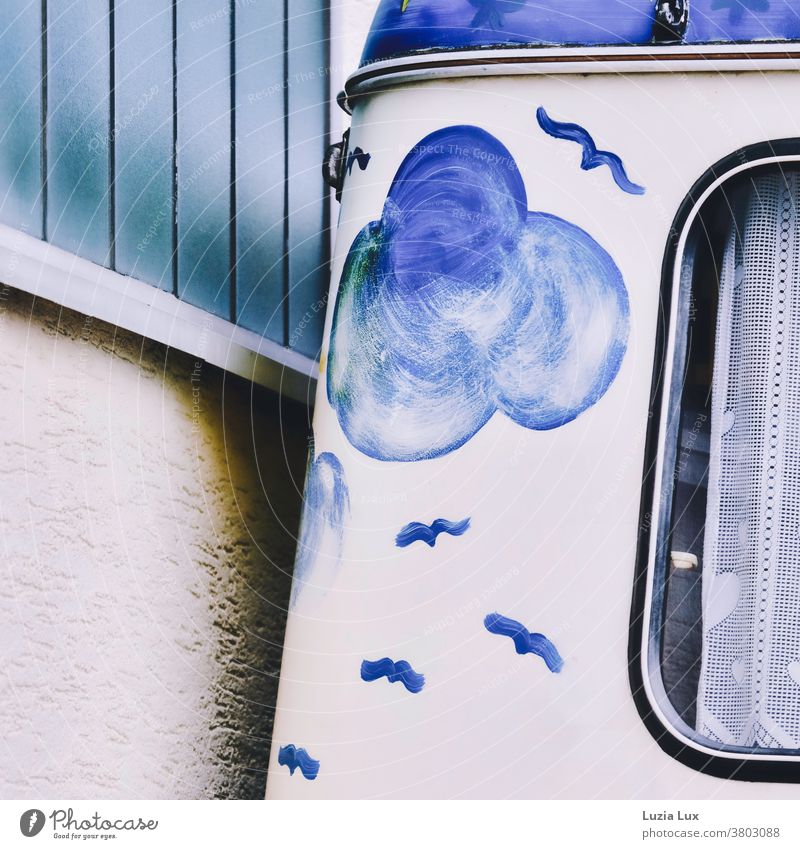 Ausflugsstimmung, blau und nostalgisch: ein alter, schön bemalter Wohnwagen wurde dicht an einer farblich passenden Wand geparkt Wolken Vögel Vorhang Gardine