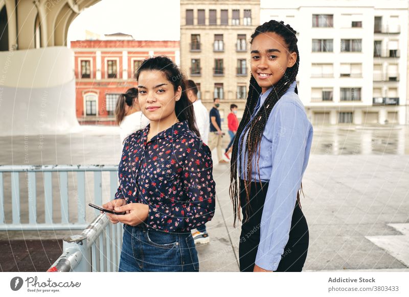 Crop fröhlich multiethnischen Freundinnen mit Smartphone lachend auf dem Bürgersteig Lachen reden Freundschaft Schüler herzlich Straßenbelag Großstadt Lächeln