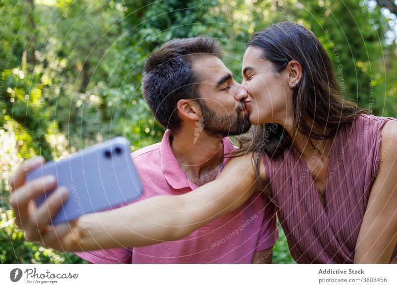 Fröhliches ethnisches Paar nimmt Selfie im Park Kuss Glück Smartphone kuscheln Termin & Datum romantisch Liebe Zusammensein Partnerschaft Apparatur Mobile