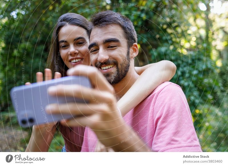 Fröhliches ethnisches Paar nimmt Selfie im Park Glück Smartphone kuscheln Termin & Datum romantisch Liebe Zusammensein Partnerschaft Apparatur Mobile Telefon