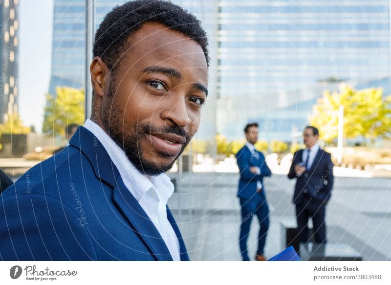 Fröhlicher schwarzer männlicher Angestellter mit Blick auf die Kamera auf der Straße Mann Optimist Lächeln selbstbewusst Business Stadtzentrum Großstadt Stil