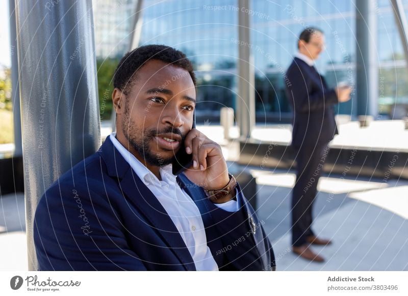 Junger schwarzer Mann, der während einer Pause auf der Straße mit seinem Smartphone spricht Telefonanruf Gespräch selbstbewusst sich[Akk] entspannen diskutieren