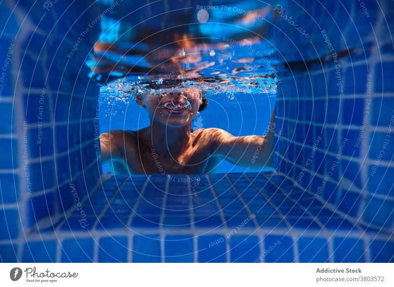 Fröhlicher Junge taucht in Poolwasser Teenager Sinkflug Schaumblase heiter unter Wasser Aktivität Lächeln Spaß sorgenfrei spielerisch platschen aqua aktiv