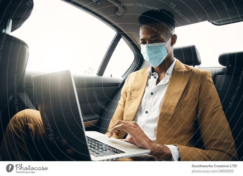 Junger Geschäftsmann mit Maske, der während einer Gesundheitspandemie am Laptop auf dem Rücksitz eines Taxis arbeitet Business Gesichtsmaske Gesichtsbedeckung