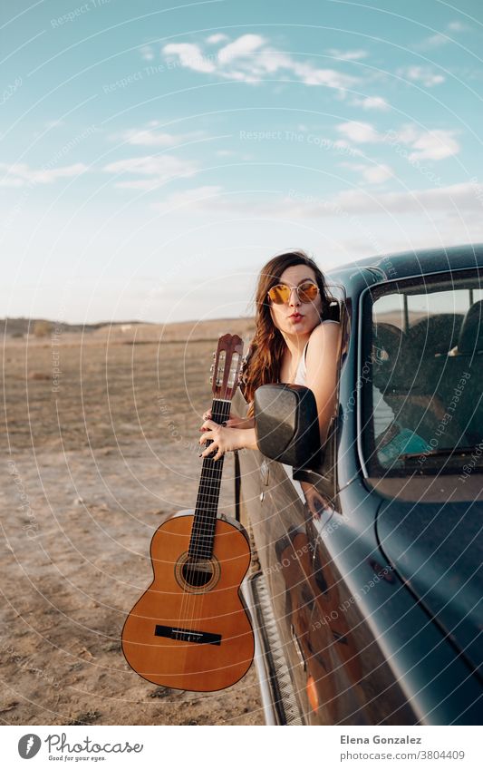 Junge reisende Frau amüsiert sich mit der Gitarre im Jeep 4x4-Auto und macht bei Sonnenuntergang einen Fernweh-Urlaub Spaß Ausflug Menschen jung altehrwürdig