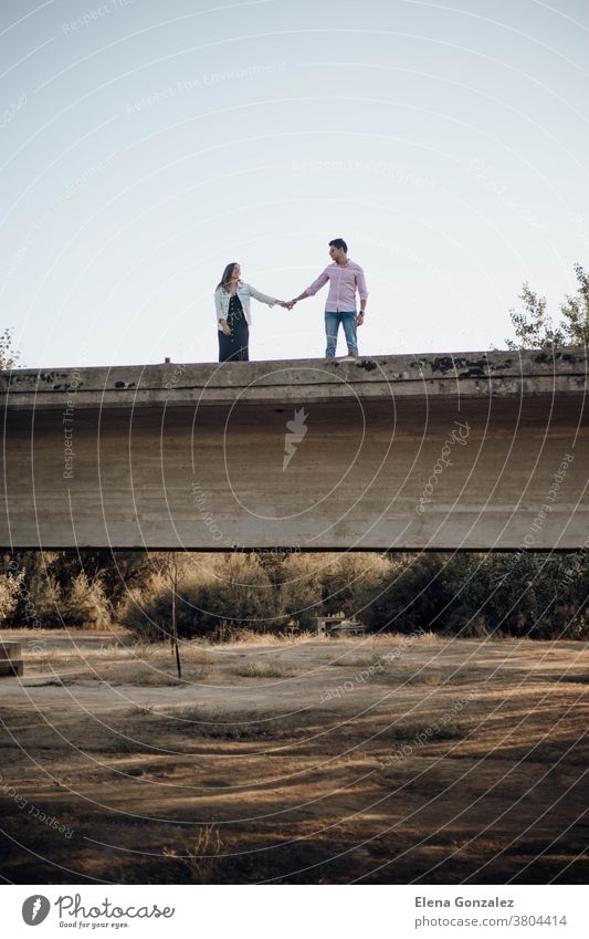 junges verliebtes Paar, das sich auf einer alten Brücke an den Händen hält Sonnenuntergang Antiquität Ruinen Halt Beteiligung Kuss Küssen Ansicht Zusammensein