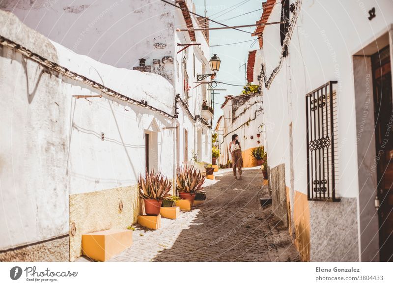 junge modische brünette Frau, die eine Straße in Elvas, Portugal, entlanggeht Weiße Straße Gelber Streifen Sommer Sommertag Töpfe Blumentöpfe farbenfroh reisen