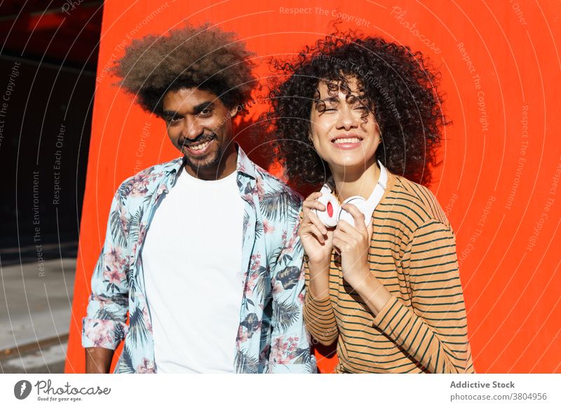 Glückliches Paar steht in der Nähe von roten Wand stylisch Afro-Look Frisur cool Zusammensein Straße hell trendy anhaben maskulin Macho Vollbart Lächeln