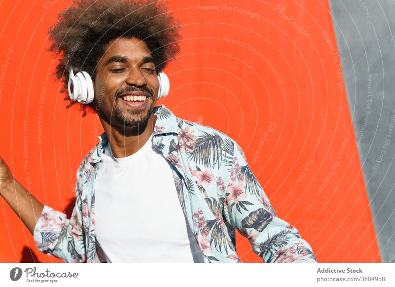 Stilvolle verträumten schwarzen Mann in modernen Kopfhörer auf der Straße stylisch zuhören Musik Augen geschlossen maskulin Afro-Look Frisur Afroamerikaner