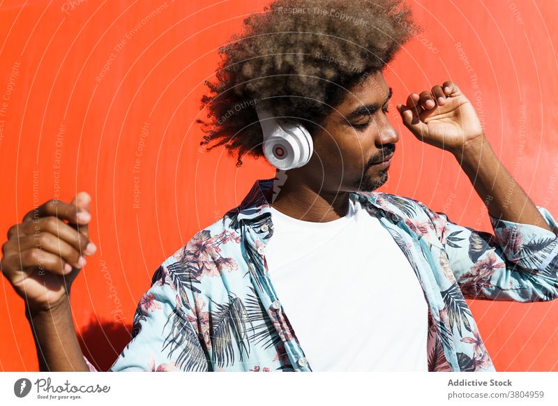 Stilvolle verträumten schwarzen Mann in modernen Kopfhörer auf der Straße stylisch zuhören Musik Augen geschlossen maskulin Afro-Look Frisur Afroamerikaner