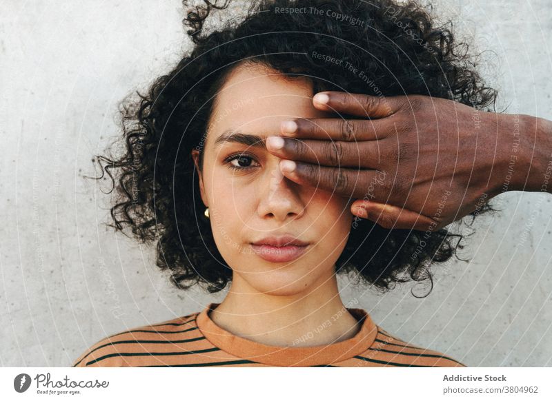 Crop-Partner, der das Auge einer schwarzen Frau in der Nähe einer Zementwand bedeckt Auge abdecken Freund Fokus stylisch Vorschein krause Haare Frisur achtsam