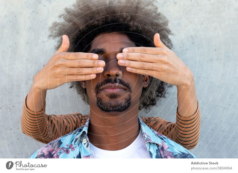 Anonymer Partner, der die Augen eines schwarzen Mannes in der Nähe einer Zementwand abdeckt Augen abdecken Freund Fokus stylisch Vorschein Afro-Look Frisur