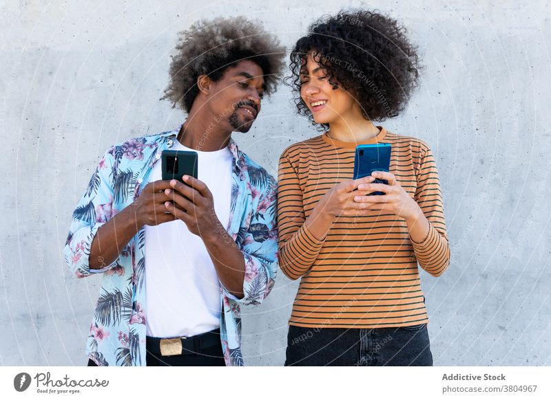 Glückliche multiethnische Freunde, die Smartphones auf der Straße beobachten Paar zuschauend Inhalt stylisch anhaben Frisur Freundschaft benutzend Apparatur