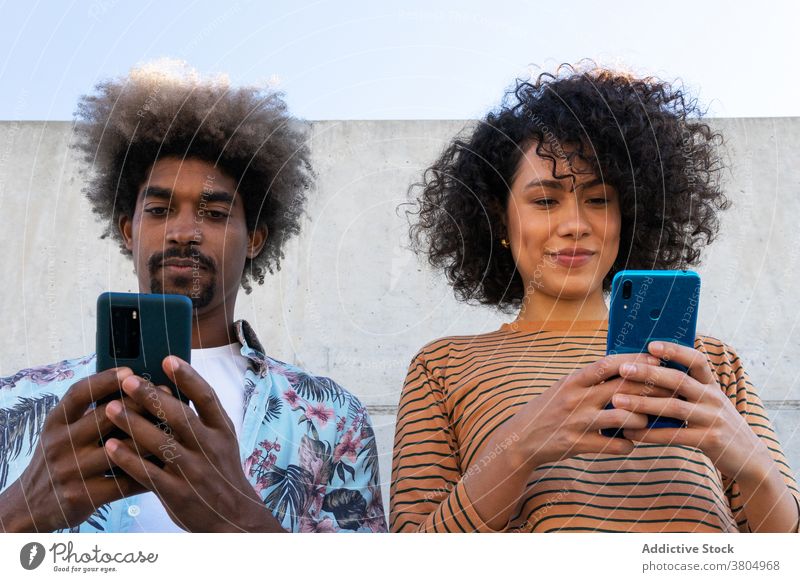 Glückliche multiethnische Freunde, die Smartphones auf der Straße beobachten Paar zuschauend Inhalt stylisch anhaben Frisur Freundschaft benutzend Apparatur