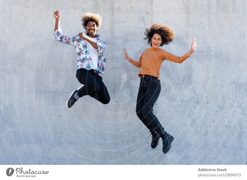 Aufgeregt diverse Freunde springen in der Nähe der Wand auf der Straße aufgeregt Spaß haben stylisch Bekleidung Glück Afro-Look Frisur trendy rassenübergreifend