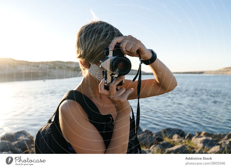 Fokussierte junge Frau mit Fotokamera entspannt auf felsigen Meeresufer bei Sonnenuntergang sich[Akk] entspannen MEER Küste Tourist Fotoapparat friedlich