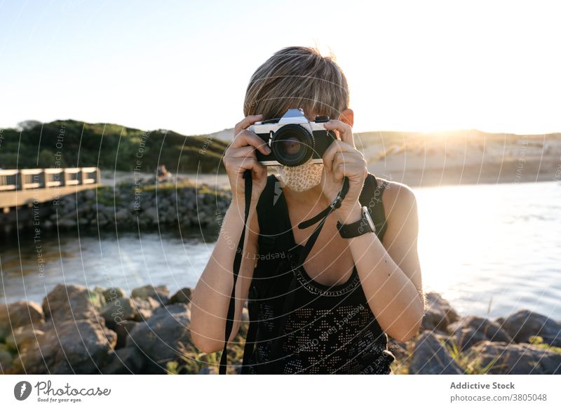 Fokussierte junge Frau mit Fotokamera entspannt auf felsigen Meeresufer bei Sonnenuntergang sich[Akk] entspannen MEER Küste Tourist Fotoapparat friedlich