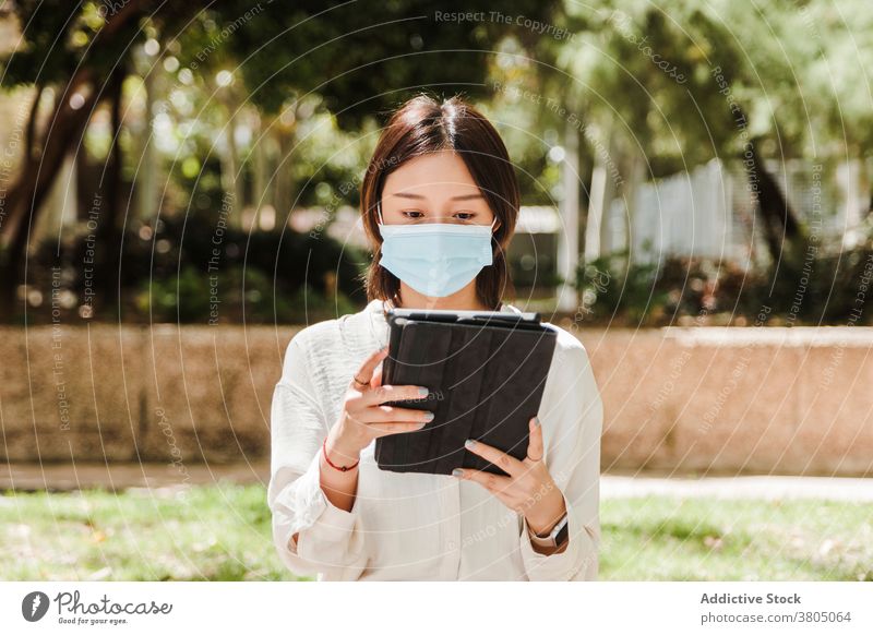 Junge ethnische Frau arbeitet aus der Ferne auf Tablet im Park Arbeit Tablette abgelegen achtsam neue Normale Coronavirus Job beschäftigt Apparatur benutzend