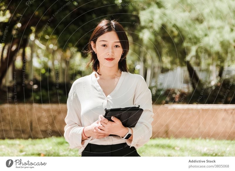 Lächelnde asiatische Geschäftsfrau mit Tablette im Park Frau positiv Unternehmer Arbeit Job Stil selbstbewusst professionell jung ethnisch formal Gerät modern