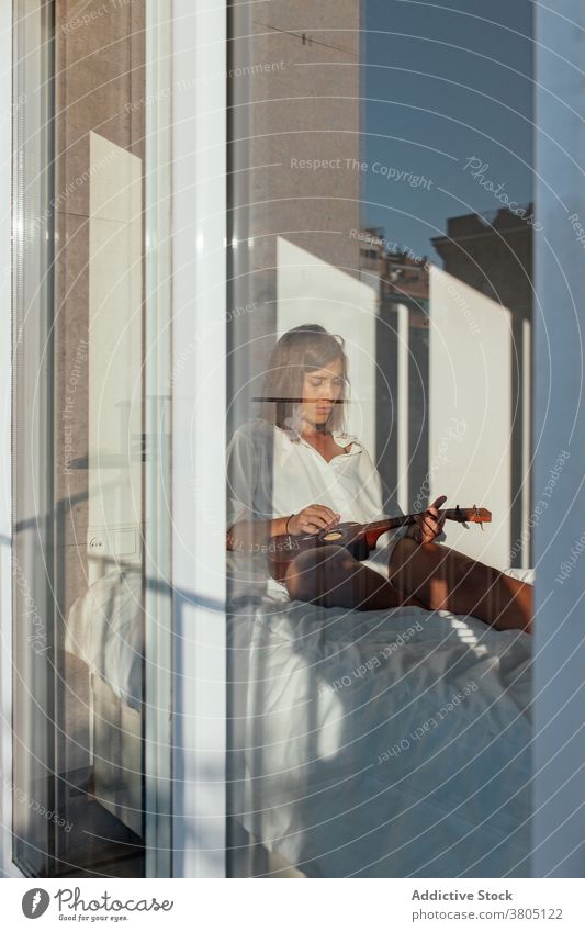 Sinnliche Frau legt Ukulele auf Bett spielen Verlockung sinnlich Musiker Gesang ausführen ruhen Komfort Morgen jung traumhaft weißes Hemd Melodie genießen