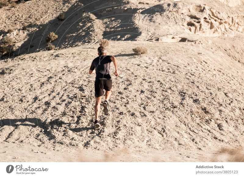 Anonymer Sportler beim Joggen auf sandigem Untergrund in bergigem Gelände Mann laufen Halbwüste Hügel Training aktiv Jogger Gesundheit Natur Wohlbefinden Sand
