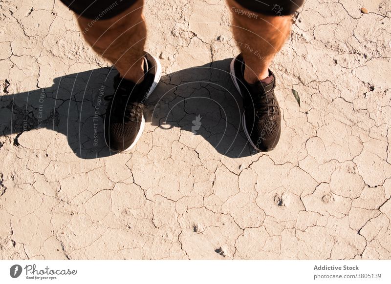 Anonymer Mann in sportlichen Schuhen steht in der Wüste nach dem Training trocken Boden wüst Stil ruhen Erholung Athlet Übung männlich Turnschuh Shorts