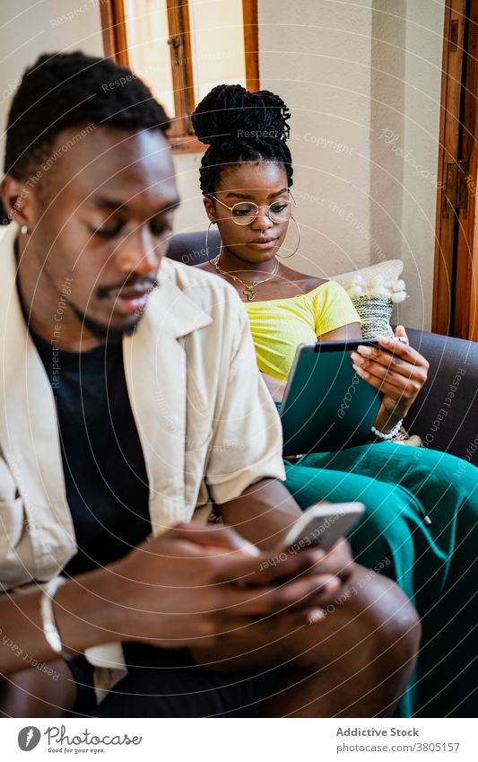 Junges ethnisches Paar verwendet Gadgets beim Entspannen auf der Couch zu Hause sich[Akk] entspannen Sofa Zusammensein Partnerschaft Tablette Smartphone