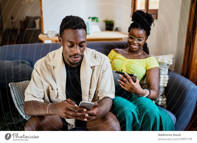 Junges ethnisches Paar verwendet Gadgets beim Entspannen auf der Couch zu Hause sich[Akk] entspannen Sofa Zusammensein Partnerschaft Tablette Smartphone