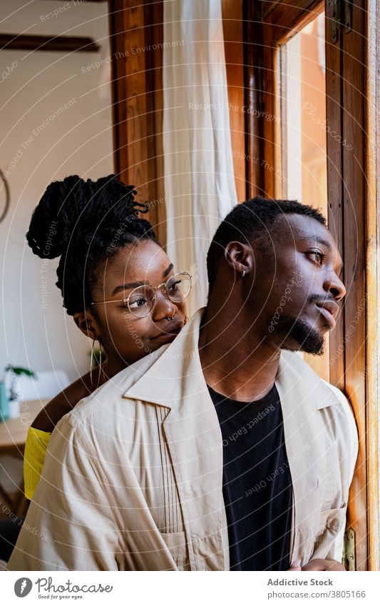 Positive schwarze Frau schaut auf nachdenklichen Ehemann im gemütlichen Zimmer Paar Zahnfarbenes Lächeln positiv besinnlich Innenbereich nachdenken Zusammensein