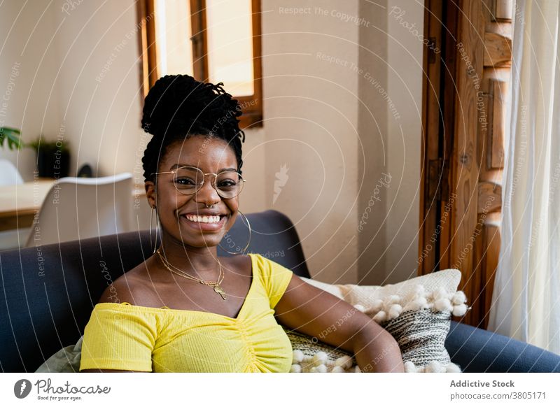 Fröhliche schwarze Frau, die sich im Wohnzimmer ausruht Zahnfarbenes Lächeln Glück zu Hause Stil Mode ruhen Wochenende Freizeit Sofa Afroamerikaner Brille