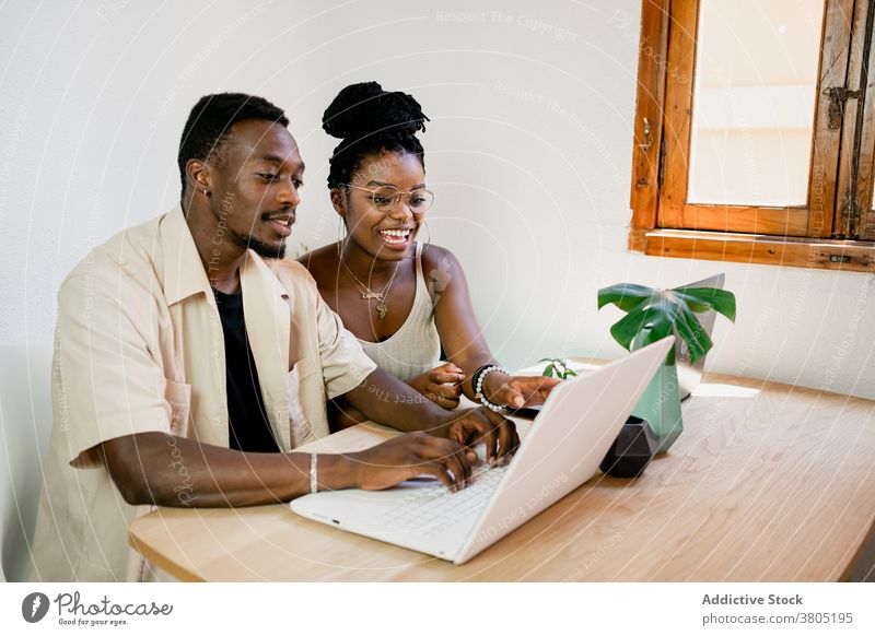 Fröhliches junges schwarzes Paar, das zu Hause per Fernzugriff an Laptops arbeitet positiv Arbeit abgelegen auf die Kamera zeigen Zusammensein Partnerschaft