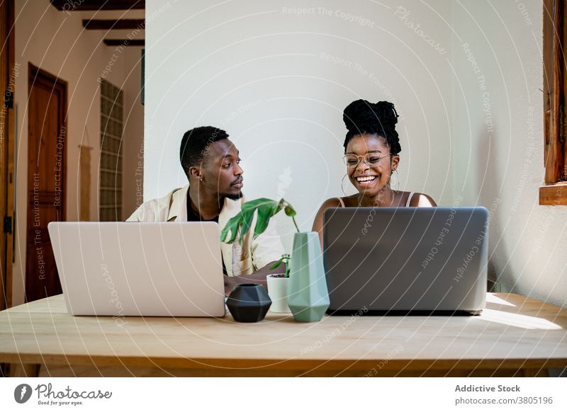 Fröhliches junges schwarzes Paar, das zu Hause per Fernzugriff an Laptops arbeitet positiv Arbeit abgelegen auf die Kamera zeigen Zusammensein Partnerschaft