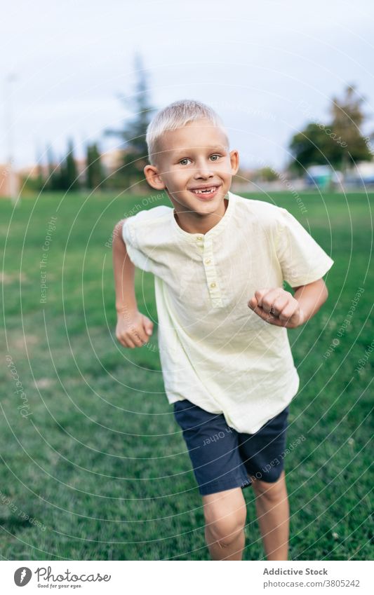 Fröhlicher Junge läuft durch den Park laufen Aktivität Zahnfarbenes Lächeln positiv heiter Wochenende spielen Spiel Sport Rasen Gras Natur sorgenfrei Inhalt