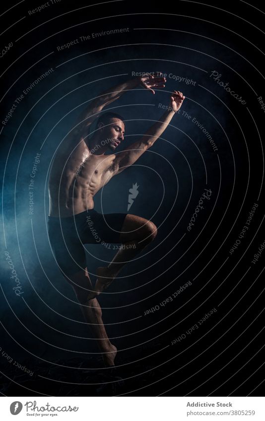 Sportliche Tänzerin Training im dunklen Raum Mann Tanzen Arm angehoben Bewegung ausführen Probe Energie expressiv muskulös neonfarbig männlich ohne Hemd