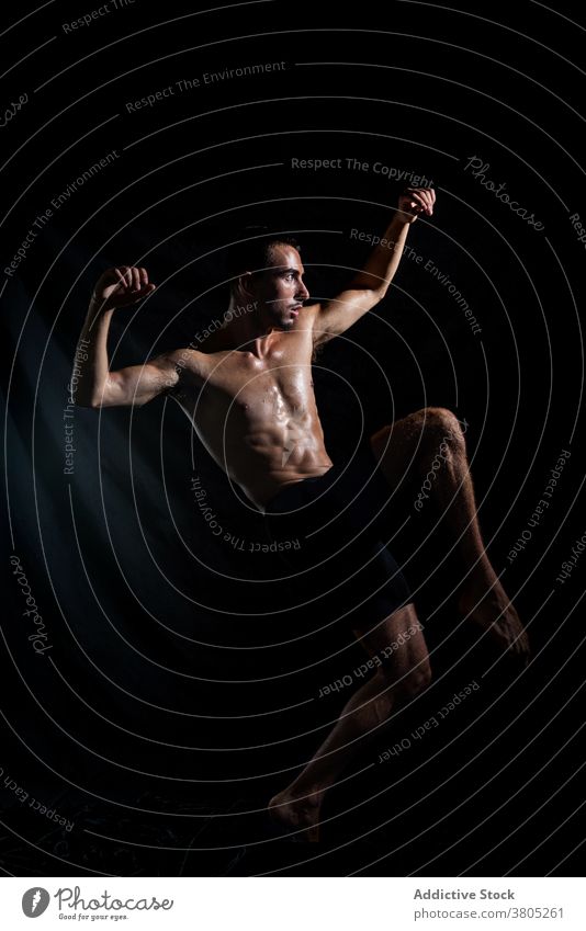 Sportliche Tänzerin Training im dunklen Raum Mann Tanzen Arm angehoben Bewegung ausführen Probe Energie expressiv muskulös neonfarbig männlich ohne Hemd