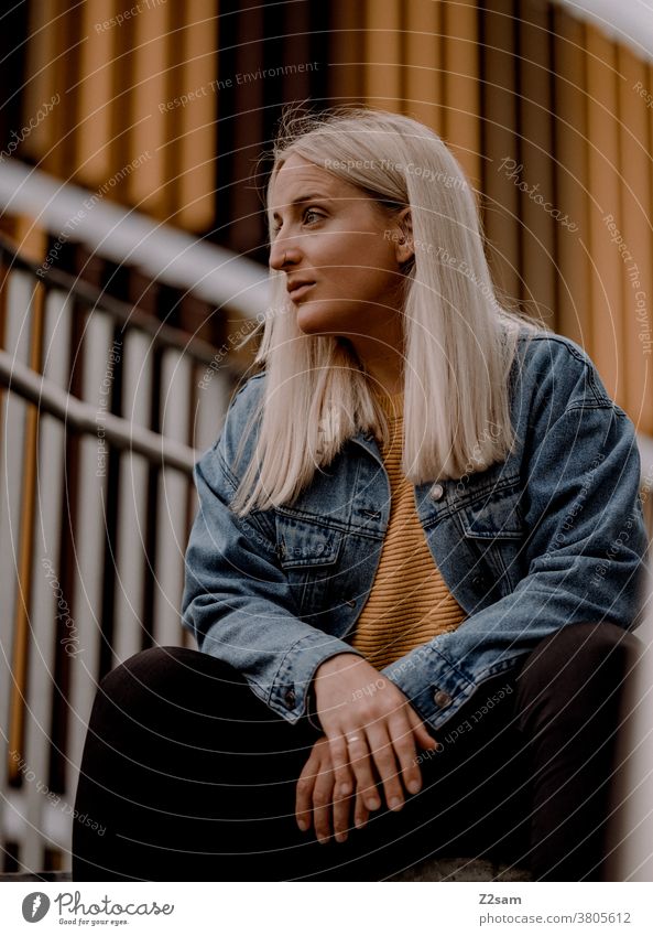 Junge blonde Frau sitzt auf der Treppe im urbanen Raum jeansjacke lange haare Lifestyle Porträt hübsch schoen Erholung selbstbewusst Stadt innenstadt orange