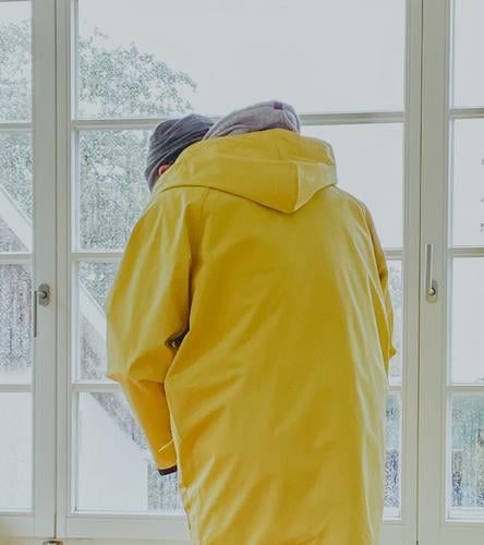 Mann steht bei Regenwetter am Fenster und zieht einen Friesennerz an | gefangen in Plastik Regenjacke Regenmantel schlechtes Wetter Schietwetter gelb
