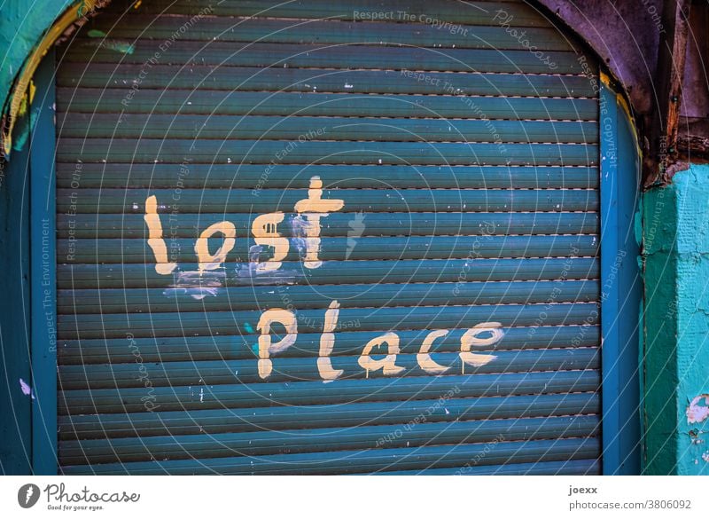 Geschlossener Eingang mit Rolladen in blau, mit Handschrift "lost Place" Lost Lost place verlassen geschlossen Wirtschaftskrise außer betrieb alt grün kaputt